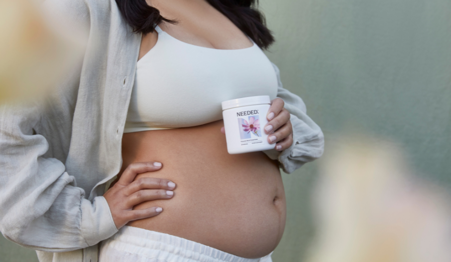 Pregnant woman holding Needed Prenatal Multi supplement in a neutral indoor setting